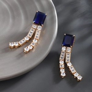 Close-up of gold-plated drop earrings with a large blue gem and sparkling zircon tassels