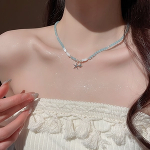 Détail de pendentifs étoile et coquillage sur un collier de perles bleu clair en œil de chat