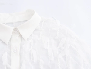 Detail shot of white shirt collar featuring elegant fringe texture and embroidery detail