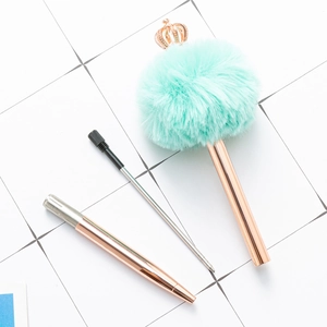 Penna a sfera in oro rosa con corona e pompon azzurro su sfondo di piastrelle bianche