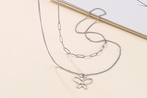 Detail of silver double-layered necklace featuring a hollow butterfly pendant and paperclip chain