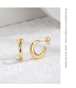 Detailed close-up of C-shaped gold-plated earrings with high-gloss finish on white fabric