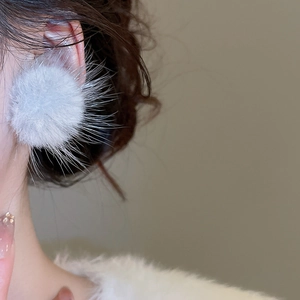 Détail de boucles d'oreilles boules de fourrure bleu clair sur modèle pour la mode hiver