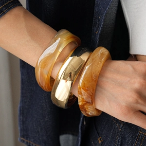 Detailed view of stacked amber acetate cuffs and gold-tone metal bangles on denim sleeve