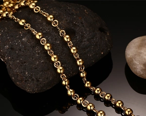 Close-up of golden beaded titanium steel chain displayed on black textured stone