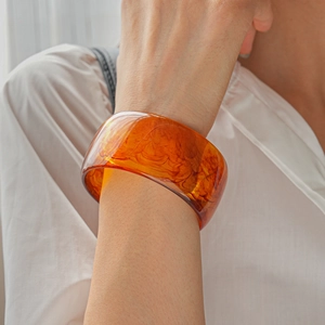 Macro detail of an amber resin bangle with a flowing texture on a model wearing white
