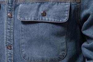 Détail de la poche de chemise en jean avec coutures contrastées et bouton en métal