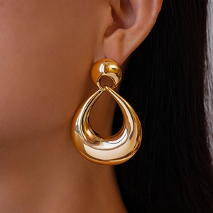 Close-up of a large golden hollow teardrop earring with smooth metallic luster on model