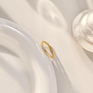 Close-up of twisted gold rope ring on white ceramic with S925 engraving detail