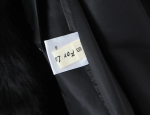 Close-up of black winter coat featuring a fluffy faux fur collar and size S interior label