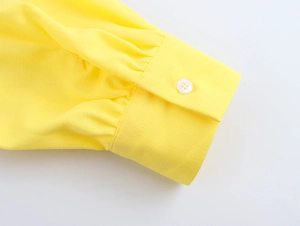 Detailed close-up of a yellow linen shirt cuff with a classic white four-hole round button