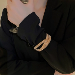 Detail of a vintage layered gold cuff bracelet styled on a black suit cuff