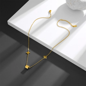 Detail showing golden stainless steel necklace with clover and cylinder charms on dark stairs