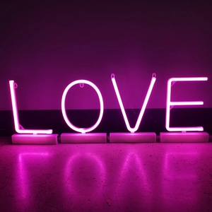 Macro detail of LOVE pink neon letter sign with white rectangular base and light reflection