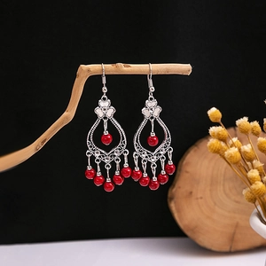 Detail view of Bohemian tassel earrings with red beads hanging on a rustic wood branch