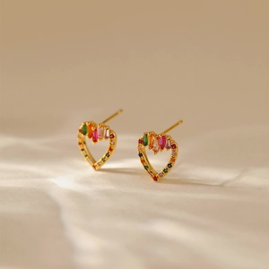 Macro detail of gold-plated heart studs featuring colorful cubic zirconia on textured fabric