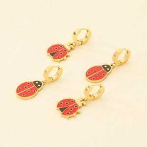 Detail showing two pairs of gold plated ladybug earrings with red enamel on fabric
