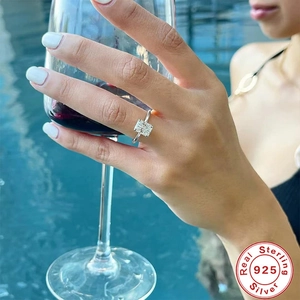 Detail of a square-cut diamond ring in 925 silver worn by a model holding wine