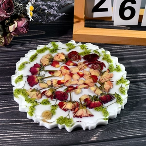Detalle de un posavasos redondo de resina con bordes ondulados y rosas rojas naturales