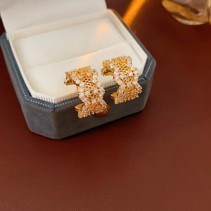 Macro shot of gold C-shaped earrings with honeycomb cutouts and pave set zircons
