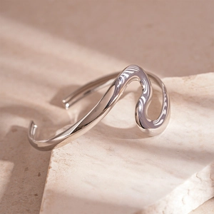Minimalist silver wavy open cuff bracelet featuring organic fluid lines on a stone base