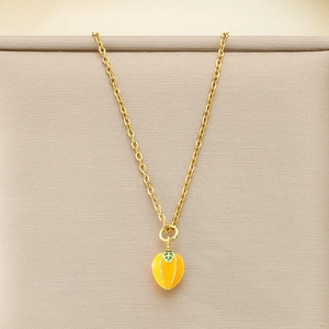 Macro shot of gold necklace with yellow mangosteen pendant and green enamel leaf detail