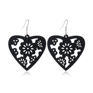 Detail of black hollow heart wood earrings with floral laser-cut patterns on white background