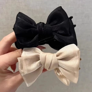 Elegant bow hair claw clips in black and champagne satin, shown in hand for size context