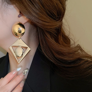 Close-up of golden geometric diamond earrings with large hollow pendant on a model