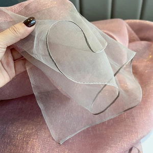 Detailed view of pink silk scarf fabric showing shimmering gold thread and fine hemmed edges