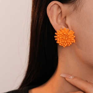 Close-up of bright orange floral firework stud earrings worn by a model in natural light