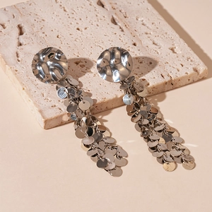 Silver metallic sequin tassel earrings with hammered texture on a stone background
