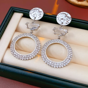 Detail of silver drop earrings with hammered metal discs and crystal rings on a soft cushion
