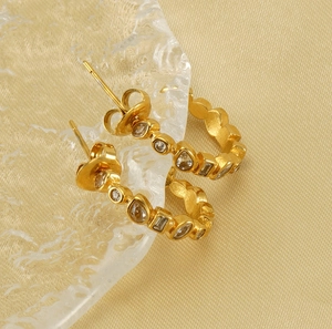Macro view of gold-plated U-shaped earrings featuring assorted clear zircon gemstones
