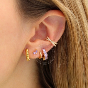 Close-up of stacked gold earrings with purple zircon butterfly and baguette crystals