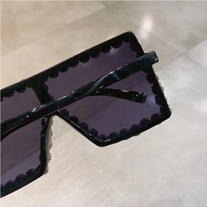 Detail view of oversized square sunglasses featuring purple lenses and beaded black frames