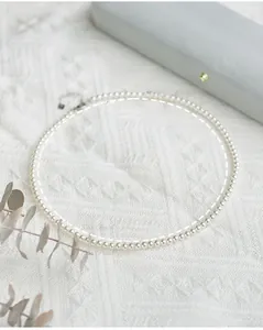 Detailed view of round white pearl necklace with silver clasp on textured fabric