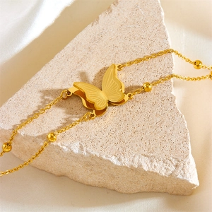 Close-up of golden butterfly bracelet with small beads resting on a beige stone surface