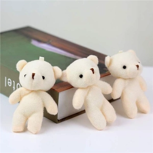 Drei kleine cremefarbene Teddybären aus Plüsch mit Aufhängeschlaufen auf einem Dekobuch