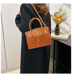Detail of a brown crocodile pattern handbag with gold metal logo and tassel decoration