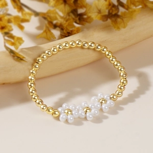 Macro detail of handmade beaded daisy flower ring with golden copper beads on beige background