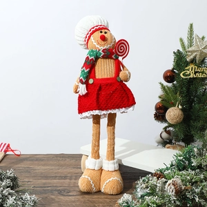 Detail of gingerbread man doll with red dress and candy cane standing near a Christmas tree