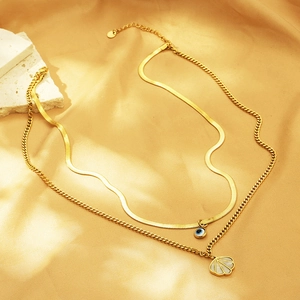 Detail of gold double-layered snake chain with evil eye and shell pendants on silk