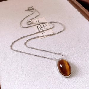 Detail of silver box chain with oval tiger eye pendant on a minimalist cream fabric