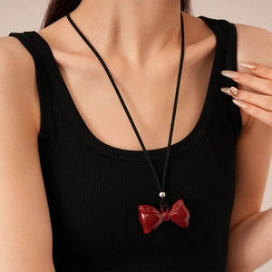 Detail of red bow resin pendant on black thin cord necklace worn by model on black tank top