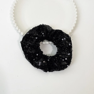 Close-up of a black sequin scrunchie and large white pearl headband on a clean white backdrop