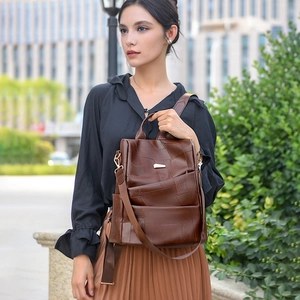 Detail of a brown leather backpack featuring a top handle and woven fabric shoulder straps