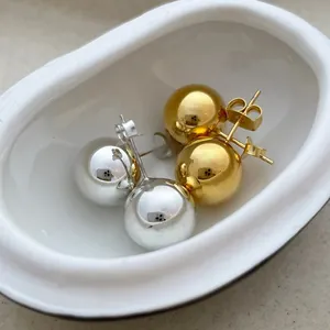 Close-up of minimalist gold and silver spherical stud earrings in a white ceramic dish