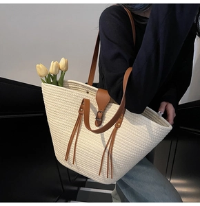 Detailed side view of large beige woven tote bag with brown leather straps on model