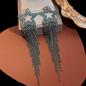 Close-up of star-shaped emerald blue rhinestone earrings with long black fringe tassels